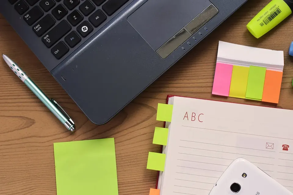 Bureau en bois vu de dessus avec un ordinateur portable, un stylo, des feuillets adhésifs de couleur et un carnet