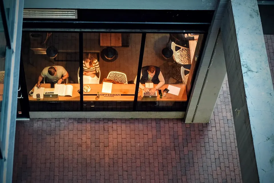 Vue plongeante sur la vitrine éclairée d'un café où travaillent des employés derrière le comptoir