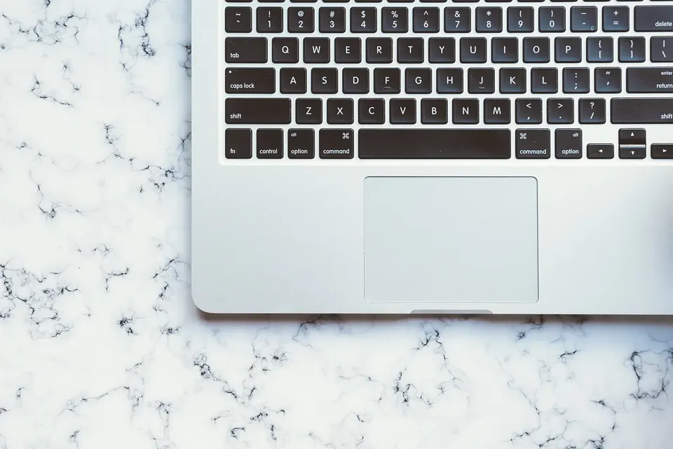 Clavier et pavé tactile d'un ordinateur portable argenté posé sur un plan de travail en marbre blanc