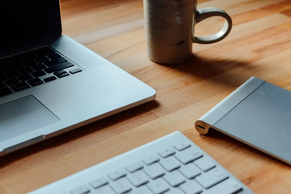 Ordinateur portable, clavier sans fil et pavé tactile sur un bureau en bois clair, avec une tasse en arrière-plan