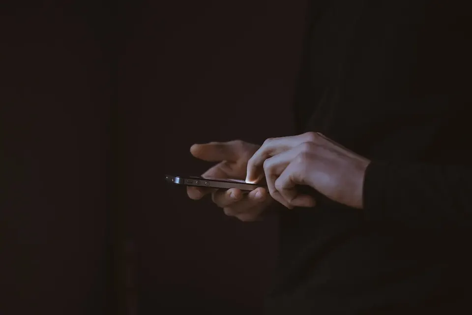 Mains tenant un smartphone allumé dans la pénombre