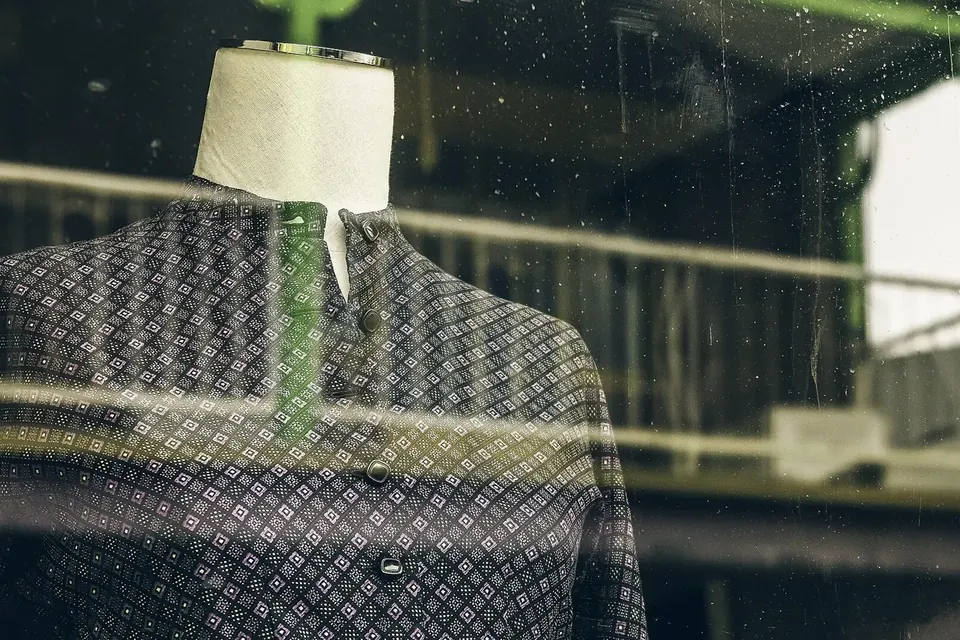 Mannequin vêtu d'une veste à carreaux derrière une vitrine où se reflète la rue